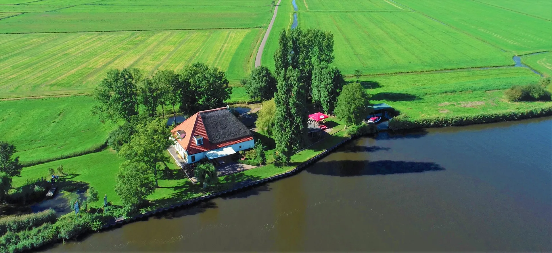 Vrijzicht vanuit de lucht: de rietgedekte woonboerderij aan het Prinses Margrietkanaal, met de eigen haven en het omliggende weiland
