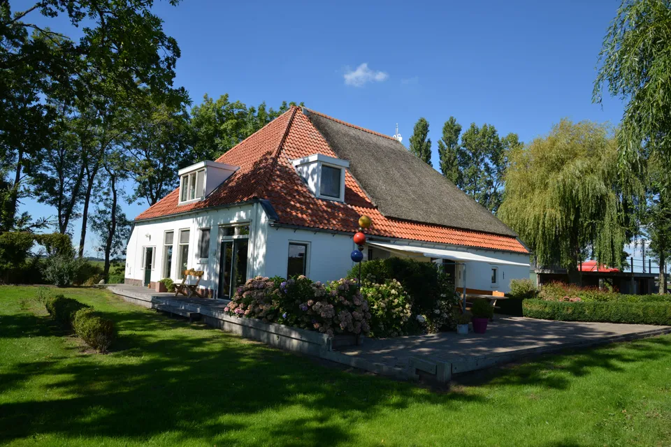 Vrijzicht in de zomer: de witte woonboerderij met rode pannen en rieten kap, gezien vanuit de tuin