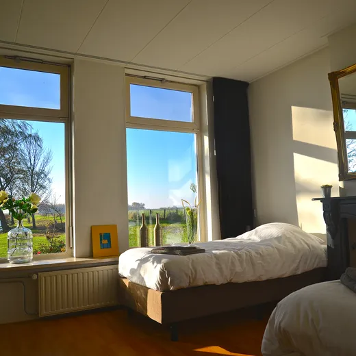 Slaapkamer met twee eenpersoonsbedden en uitzicht over het weiland en het water