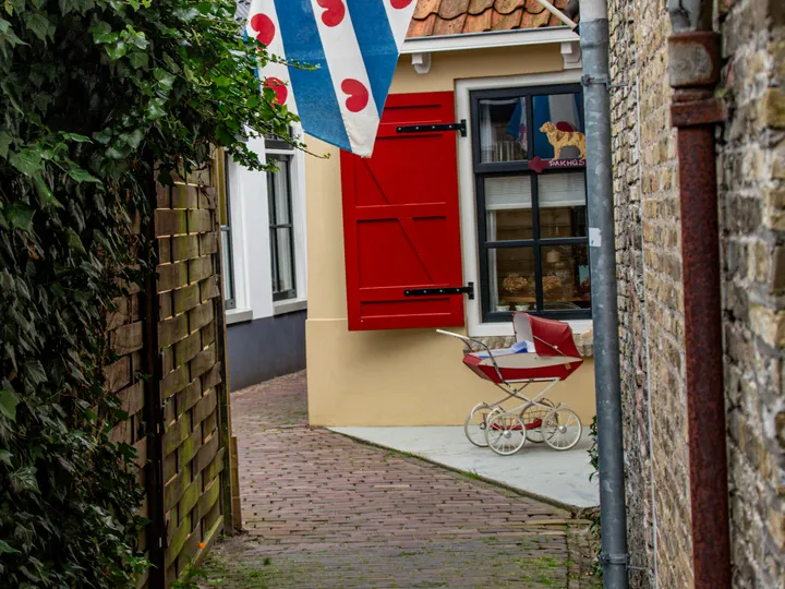 Een smal steegje met de Friese vlag, rode luiken en een oude kinderwagen